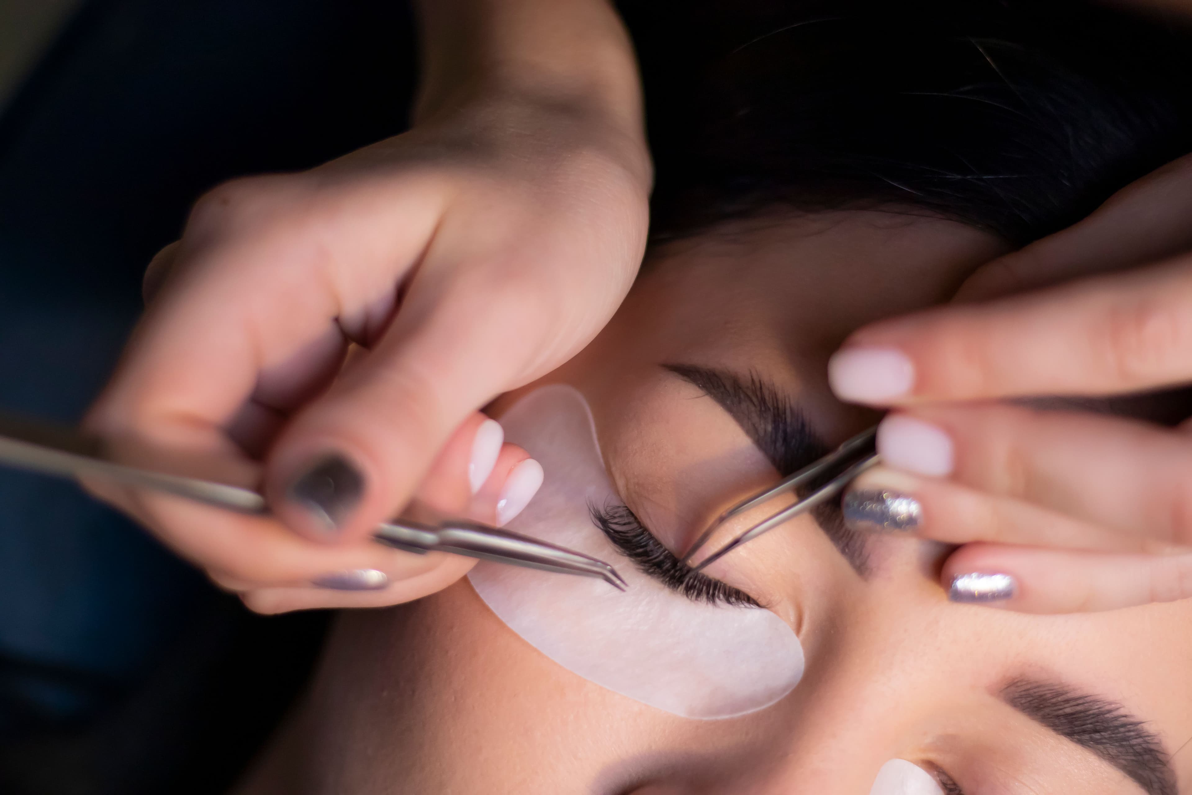 A stylist using tweezers to precisely apply eyelash extensions